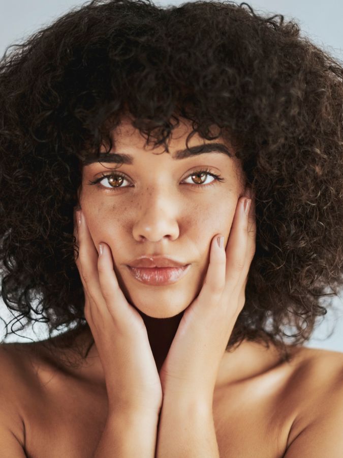 Young woman with curly hair, hands on face.